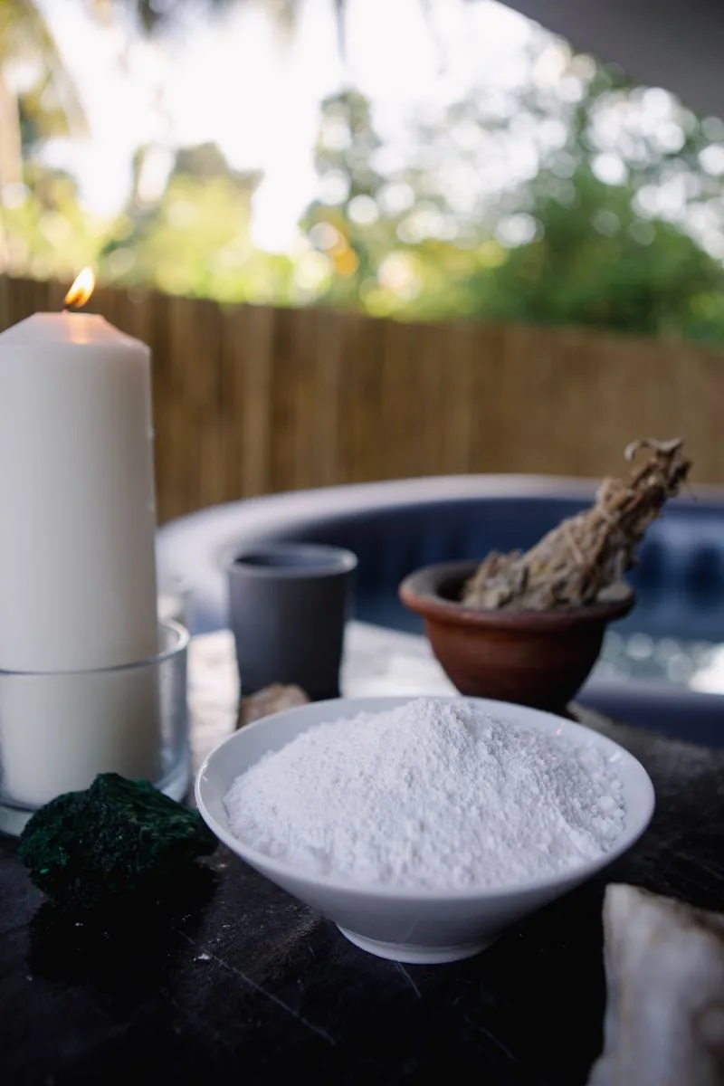 Eine weiße Schale mit Carbonatpulver vor einer Kerze und einem Salbeibündel am Rand eines Pools