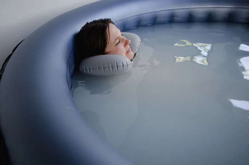 Eine Frau ruht mit Nackenkissen im milchigen Wasser eines Pools